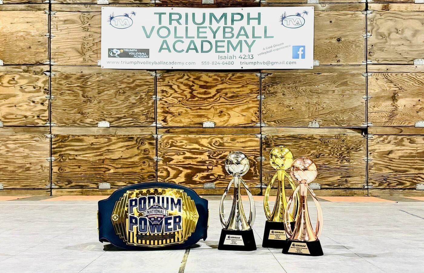Podium Power championship belt and the gold, silver and bronze trophies TVA boys won at the 2026 USA Volleyball National Championships in Phoenix, displayed under the Triumph Volleyball Academy banner